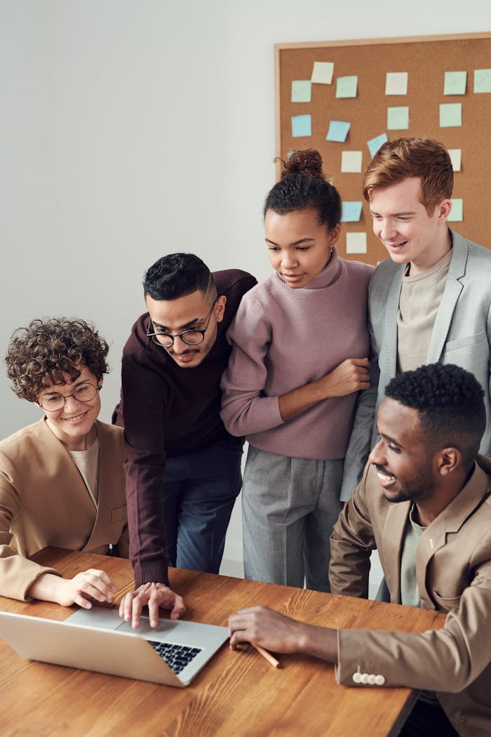 About A diverse group of young professionals collaborating around a laptop in a modern office setting.